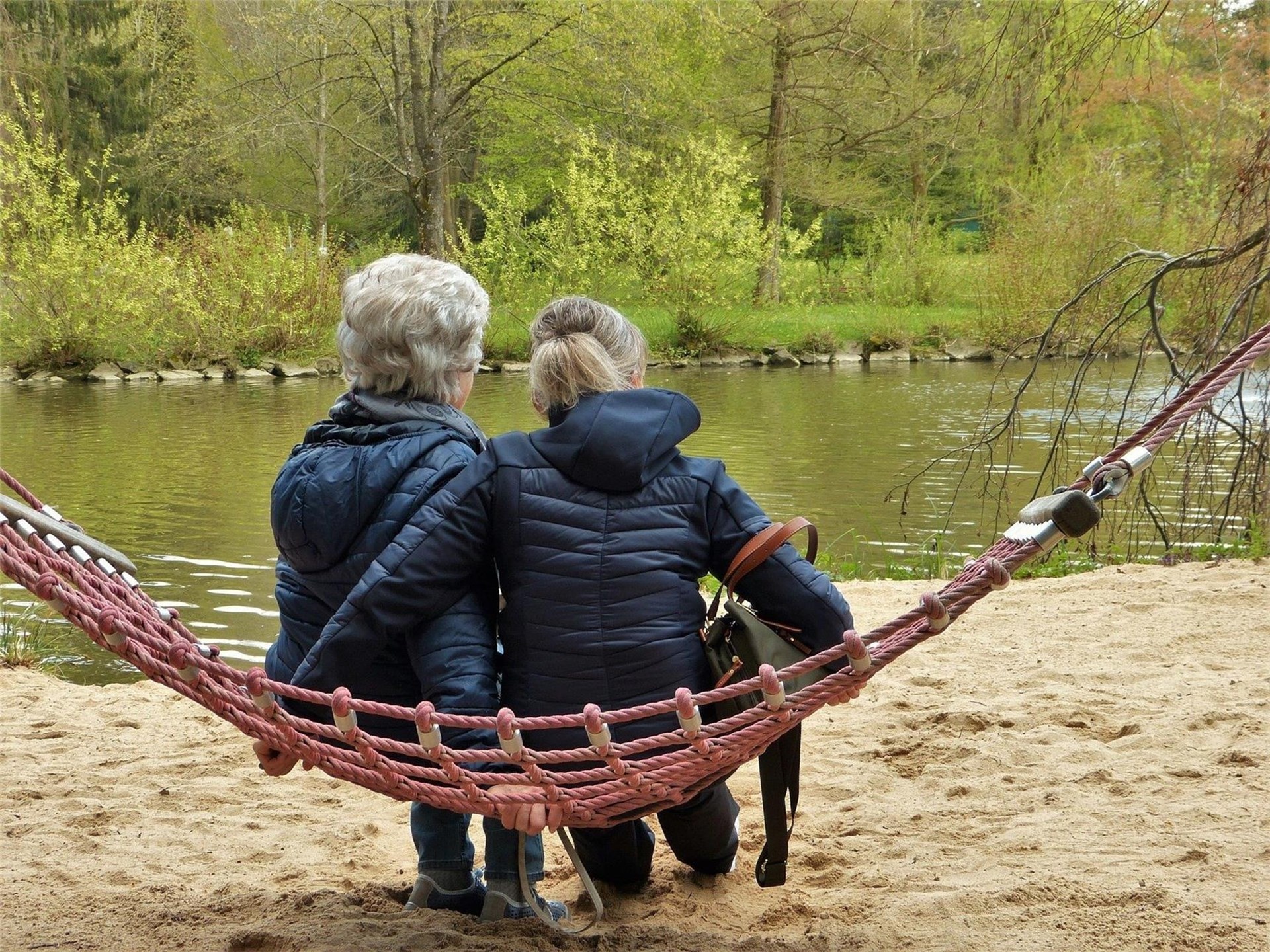Zwei Frauen sitzen nebeneinander auf einer Hängematte und schauen auf einen Fluss
